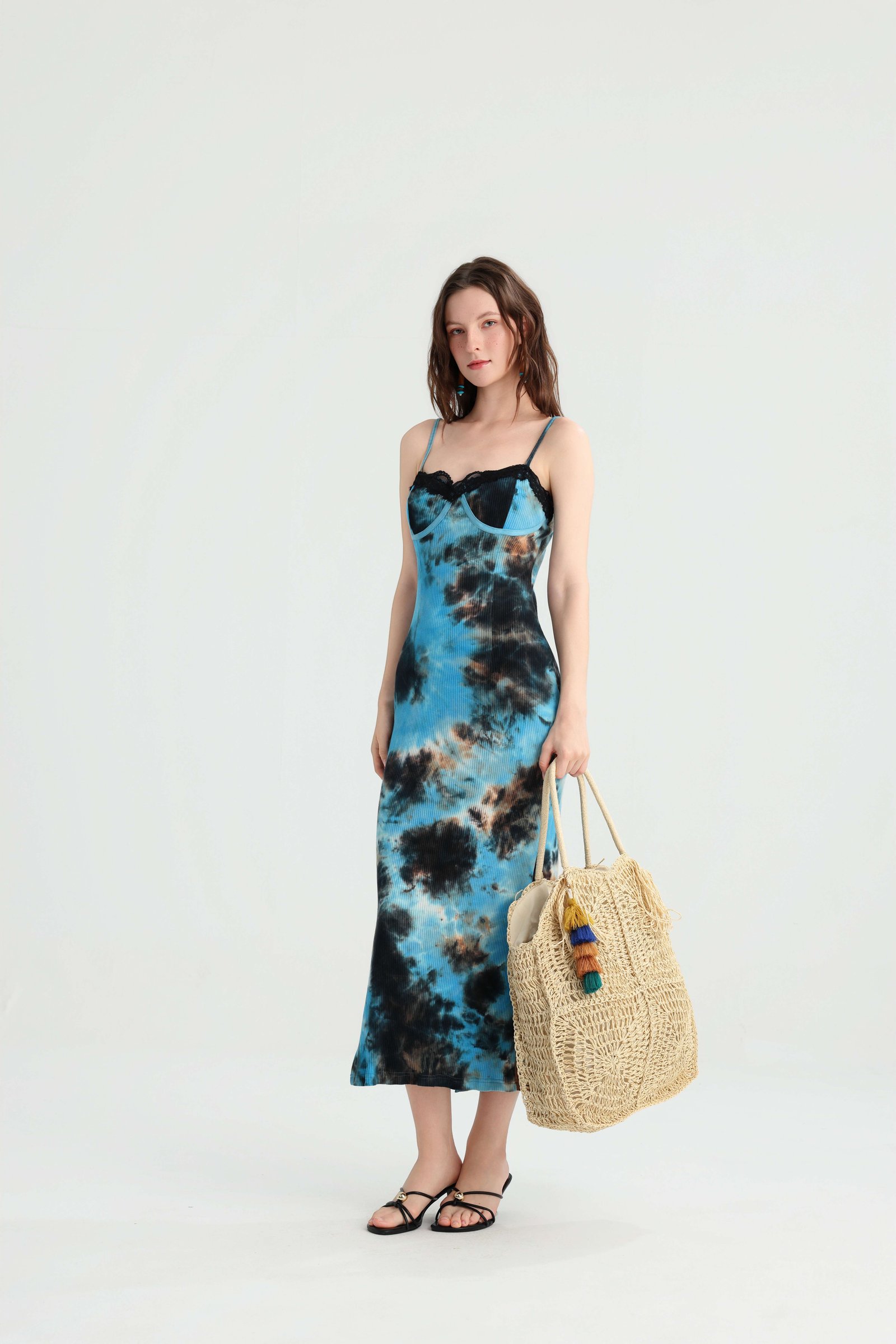 Model carrying a straw tote in a blue tie-dye vacation dress