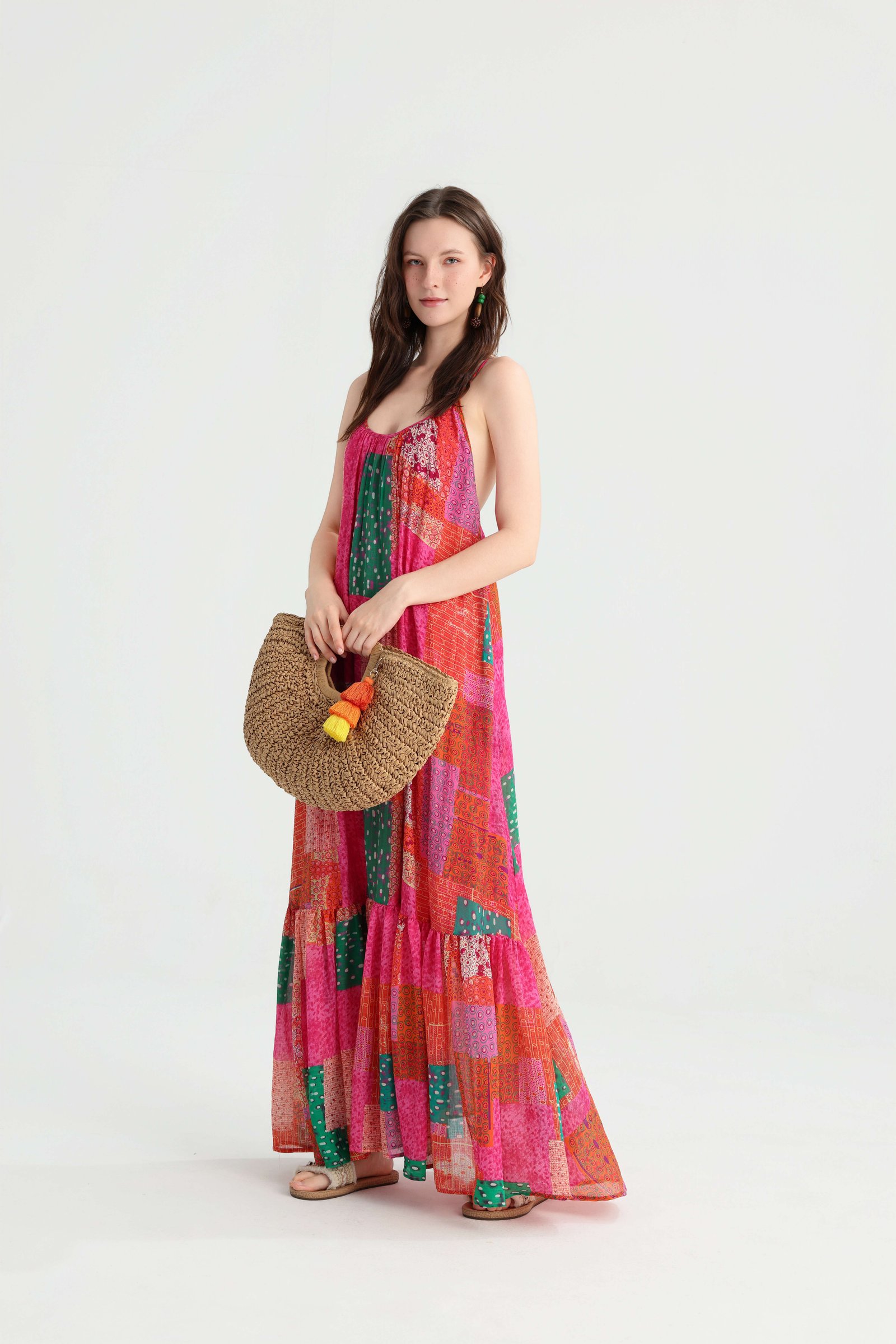 Angled front view of the colorful patchwork maxi dress styled with a rounded straw bag