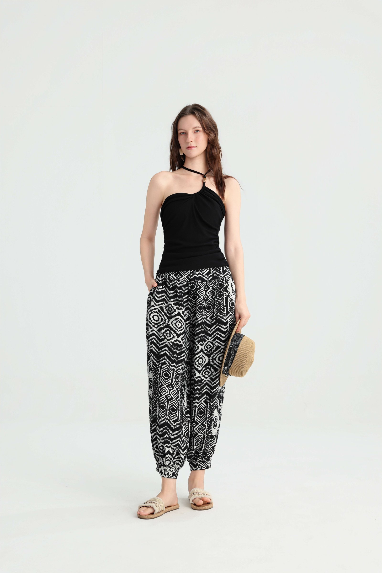 Model carrying a straw bag in a black bandeau top and harem pants