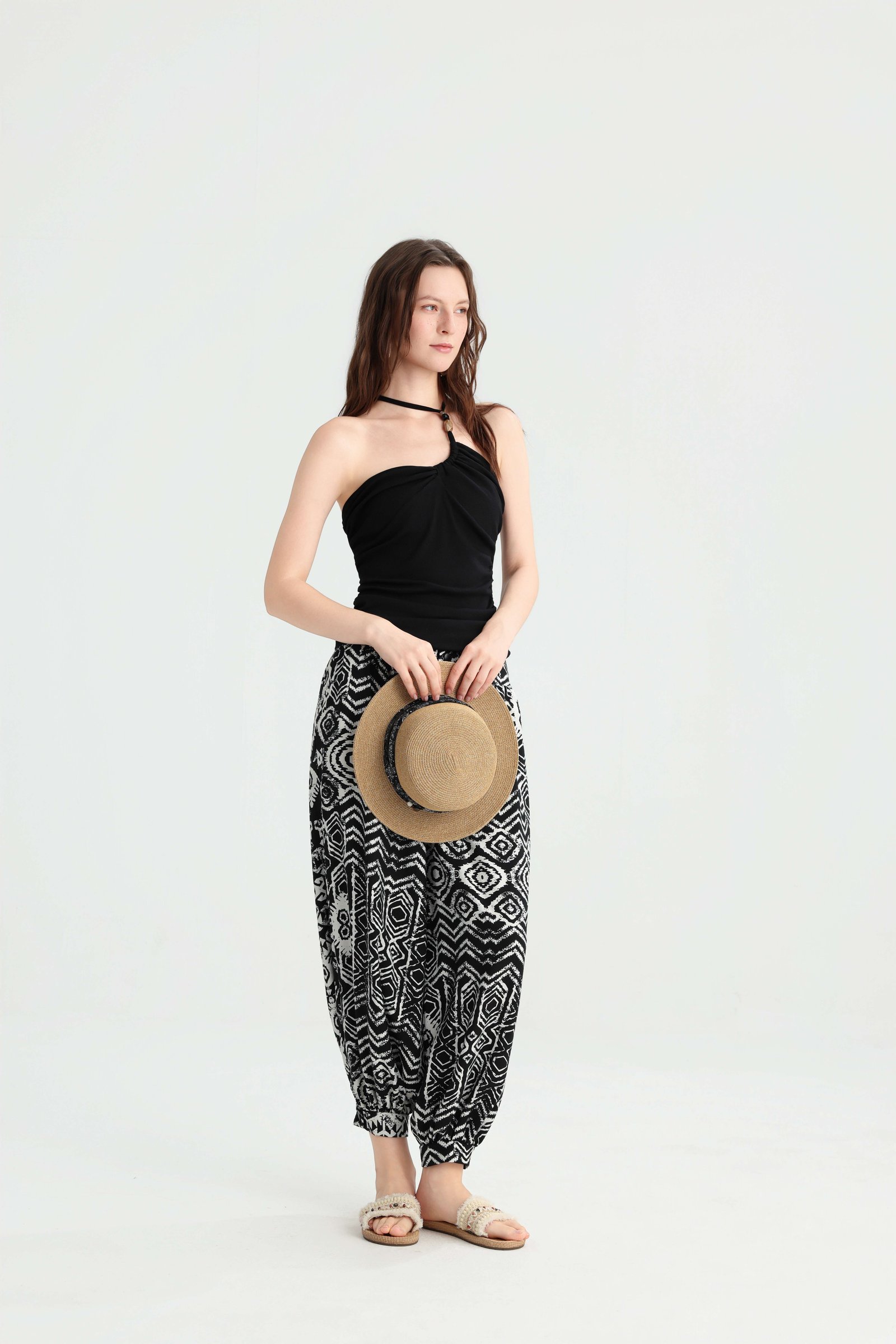 Model holding a straw hat in a black bandeau top and harem pants