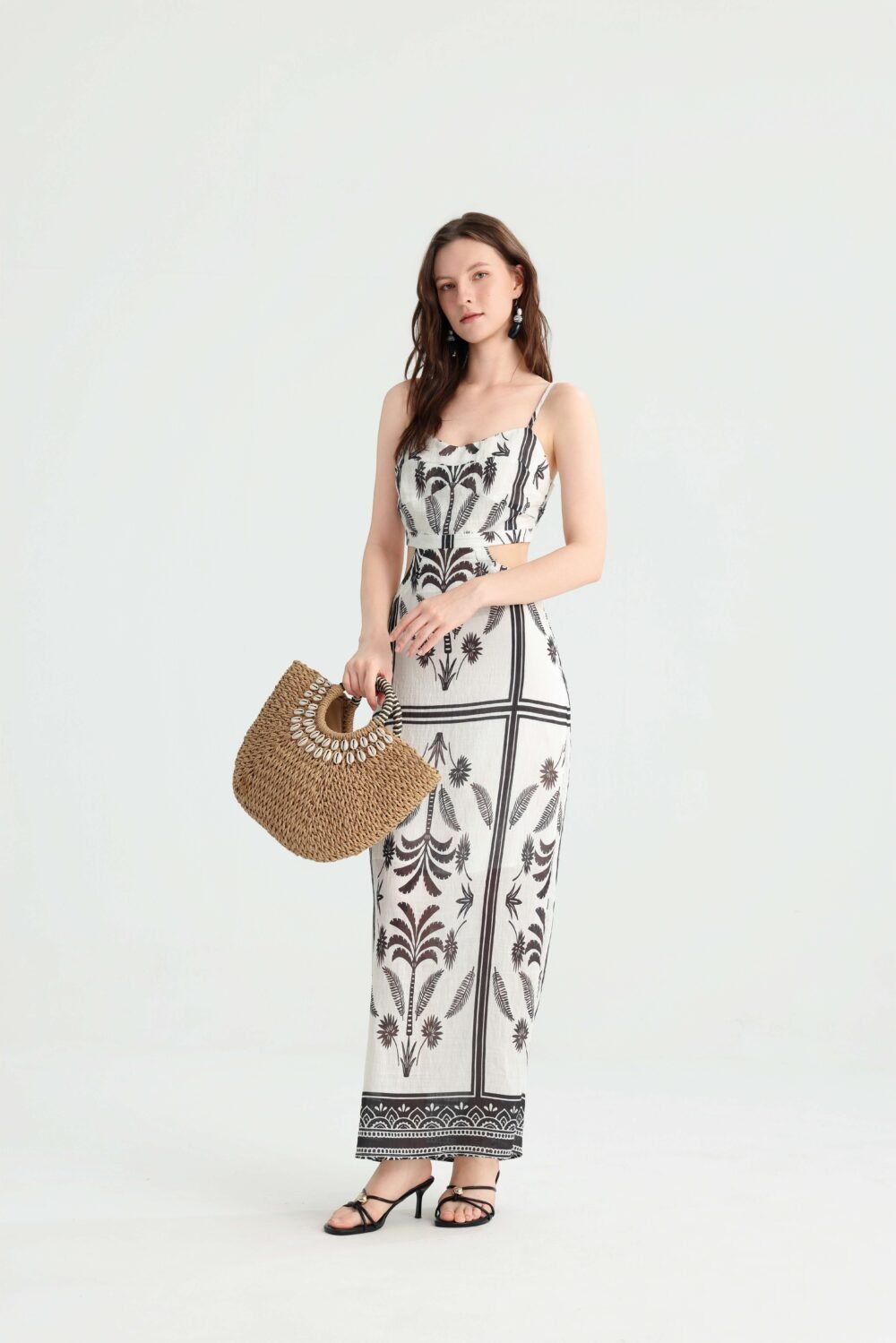 Model carrying a straw bag in an ivory palm print maxi dress